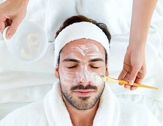 Portrait of man with clay facial mask in beauty spa.